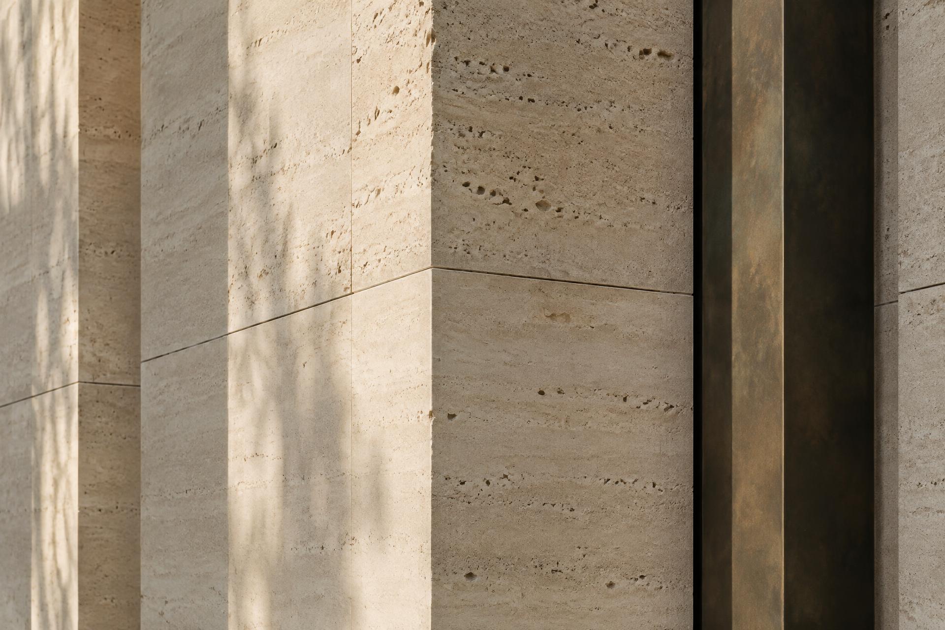 Travertine stone facade in morning light beside a bronze fin